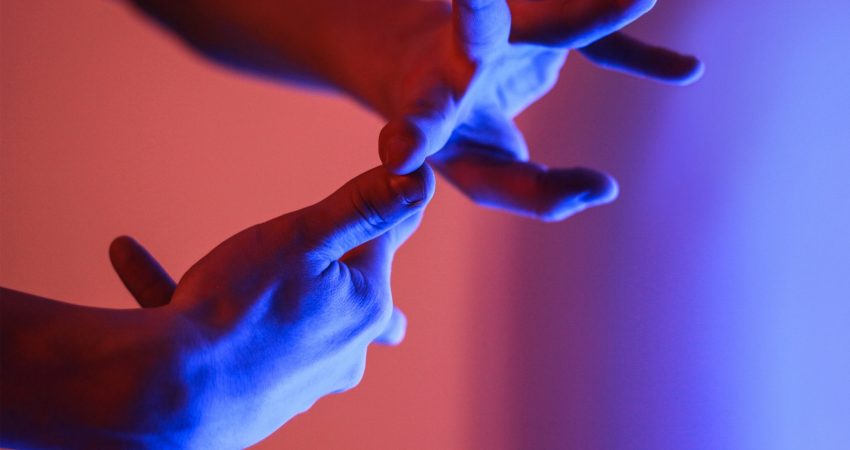 Zwei Hände formen eine Gebärde, im Hintergrund rot-blaues Licht