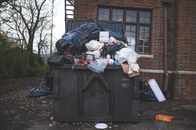 Ein überfüllter Müllcontainer vor einem Backsteingebäude.