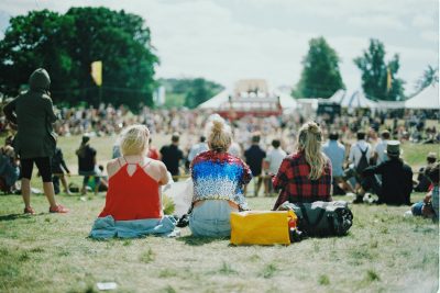 Drei Frauen sitzen nebeneinander auf einer Wiese während einer sommerlichen Festival-Veranstaltung