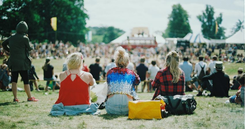 Drei Frauen sitzen nebeneinander auf einer Wiese während einer sommerlichen Festival-Veranstaltung