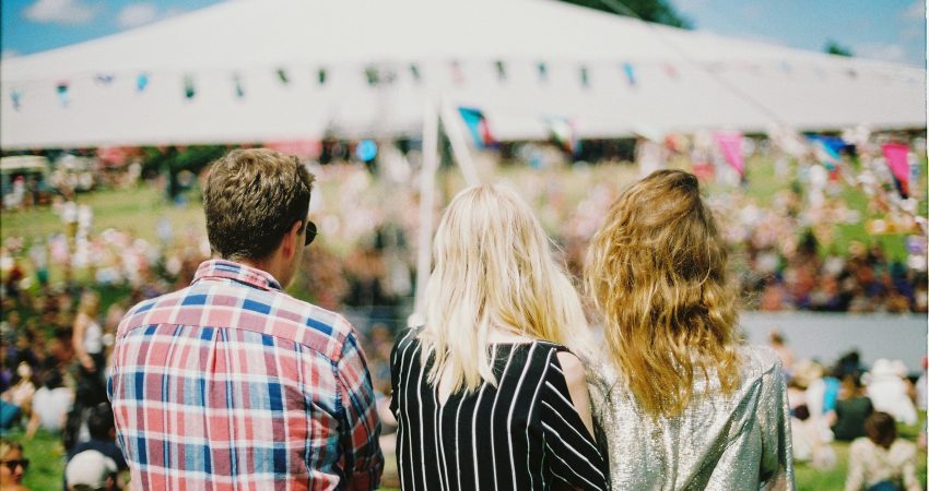Drei Menschen, die auf ein sommerliches Festival blicken.