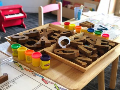 Holzbuschstabe-Bausteine und bunte Knete auf einem Kindertisch