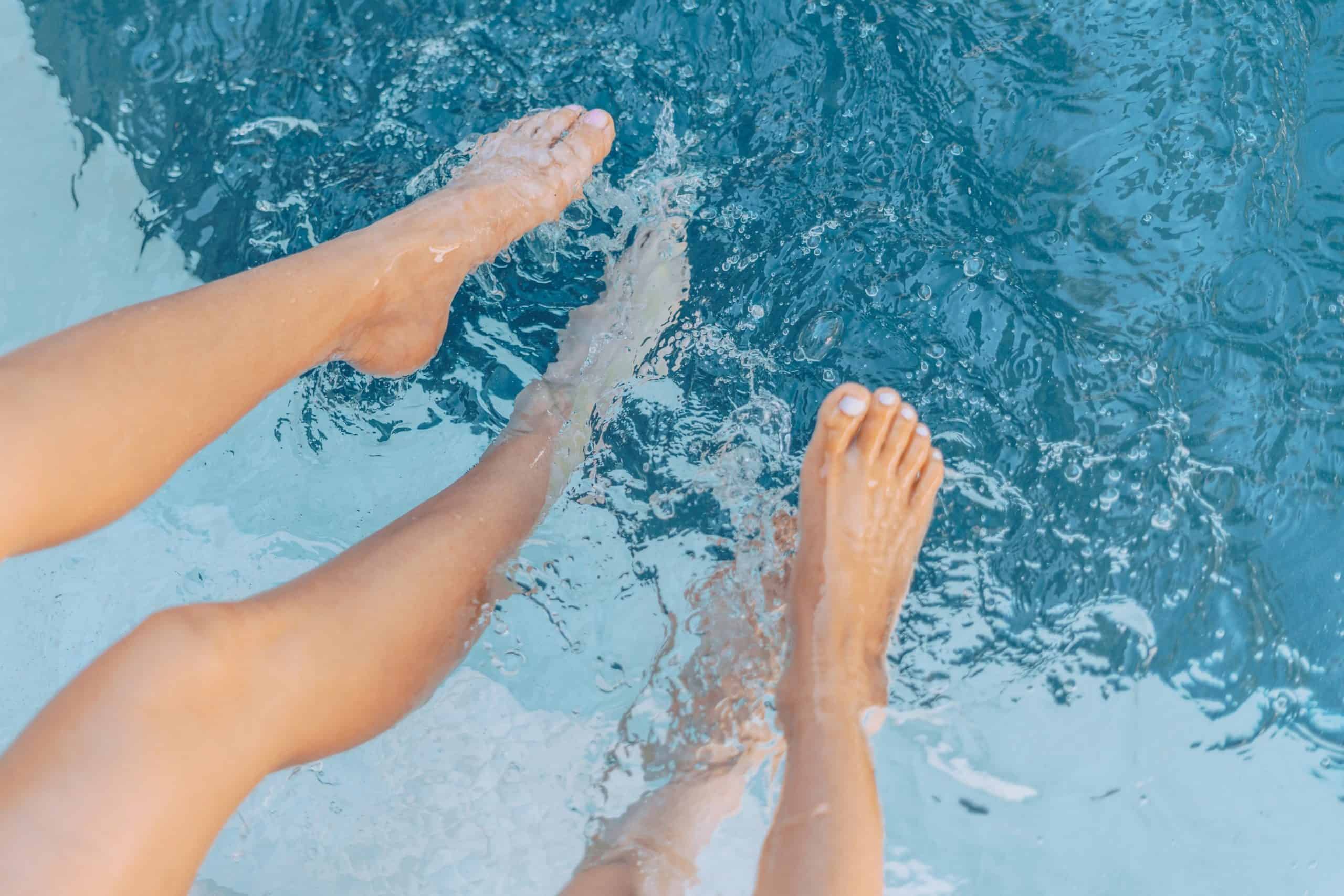 Zwei Menschen strecken die nackten Beine in ein Schwimmbecken.