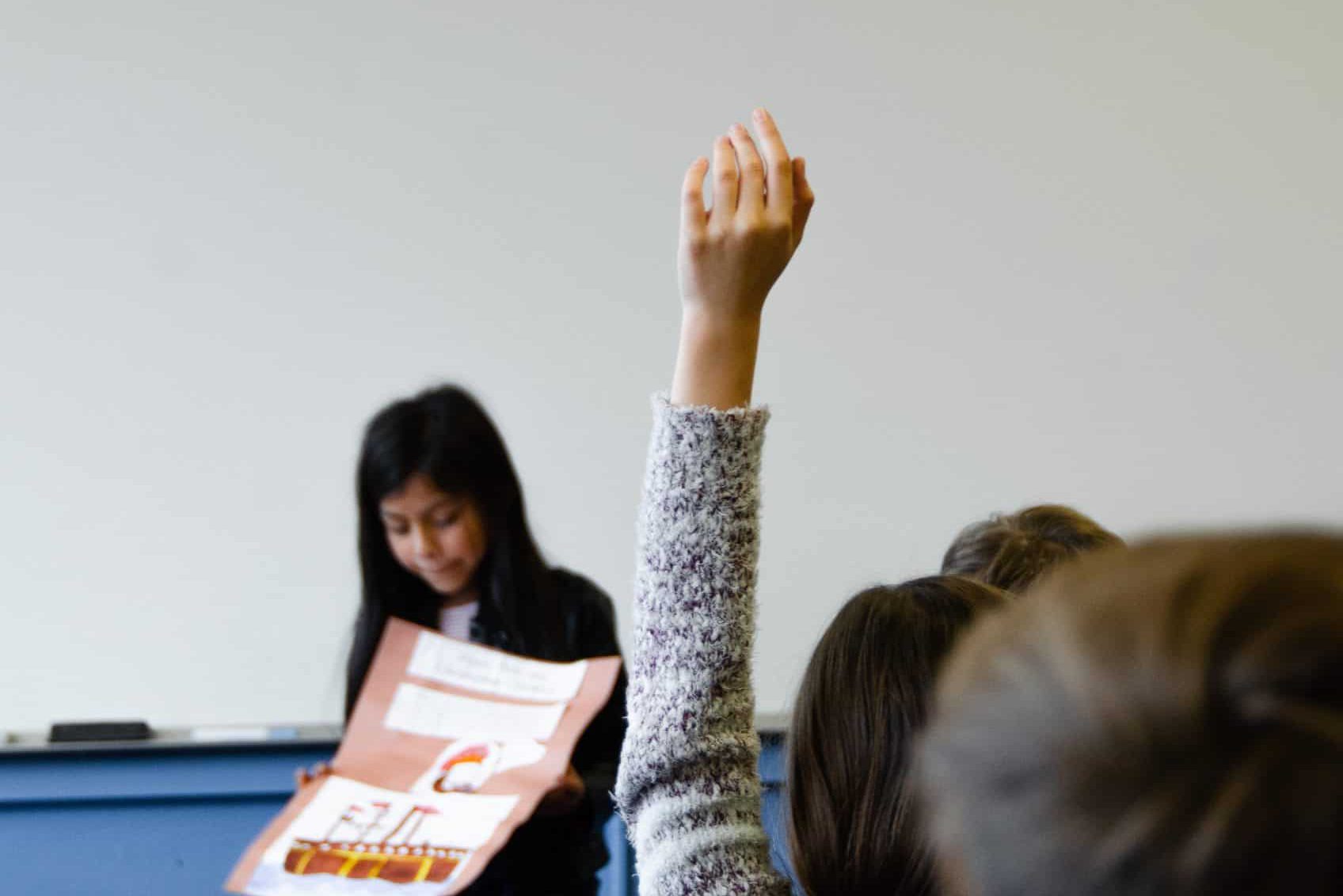 Schülerin mit Plakat in der Hand hält ein Referat vor der Klasse