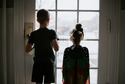 Rückenansicht eines Jungen und eines Mädchens, die vor einer verschlossenen Terrassentür stehen