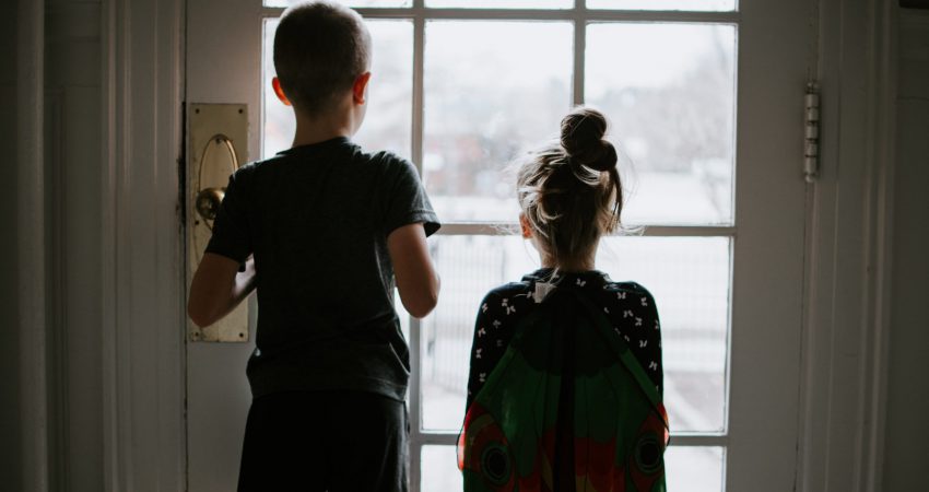 Rückenansicht eines Jungen und eines Mädchens, die vor einer verschlossenen Terrassentür stehen