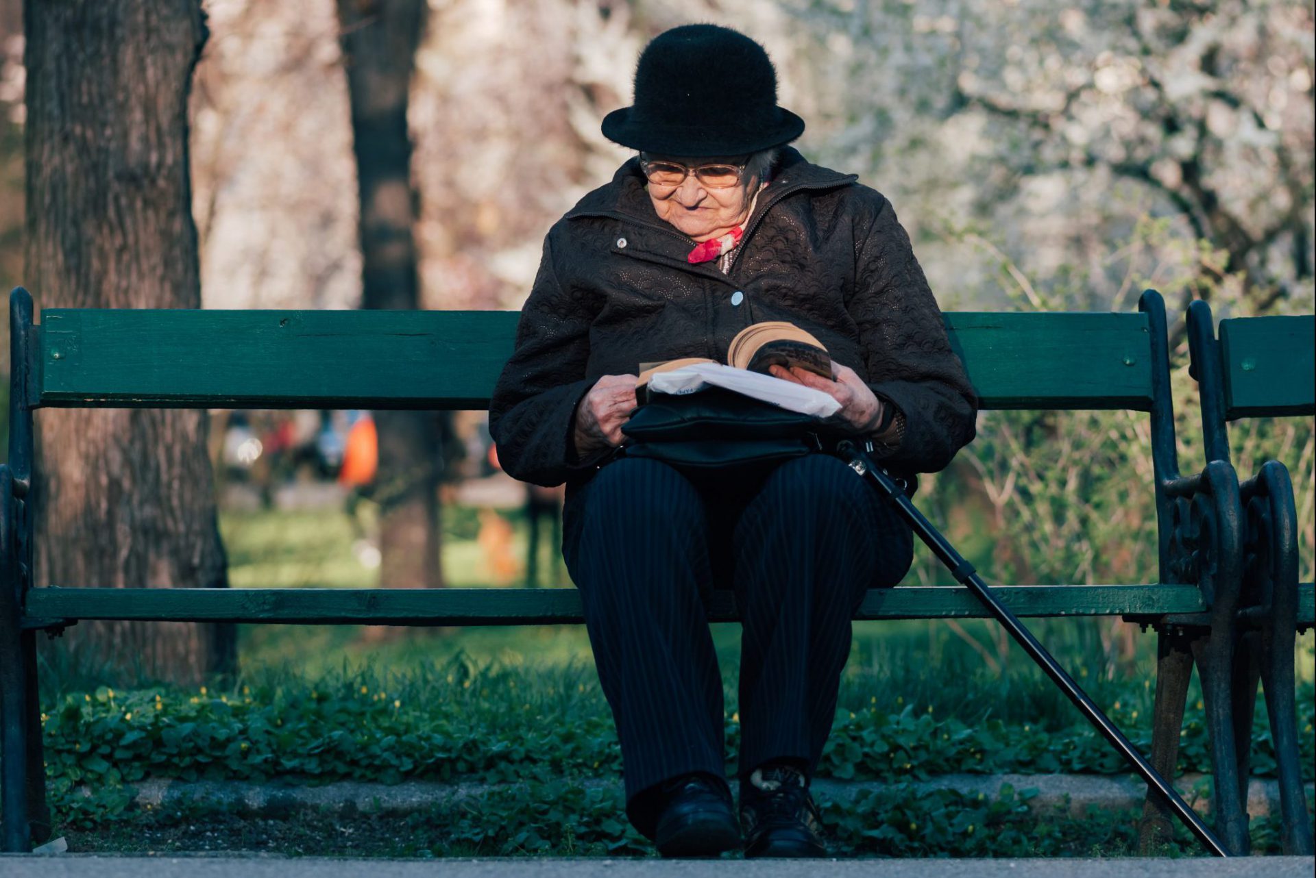 Ältere Dame mit Hut, die auf einer Parkbank liest