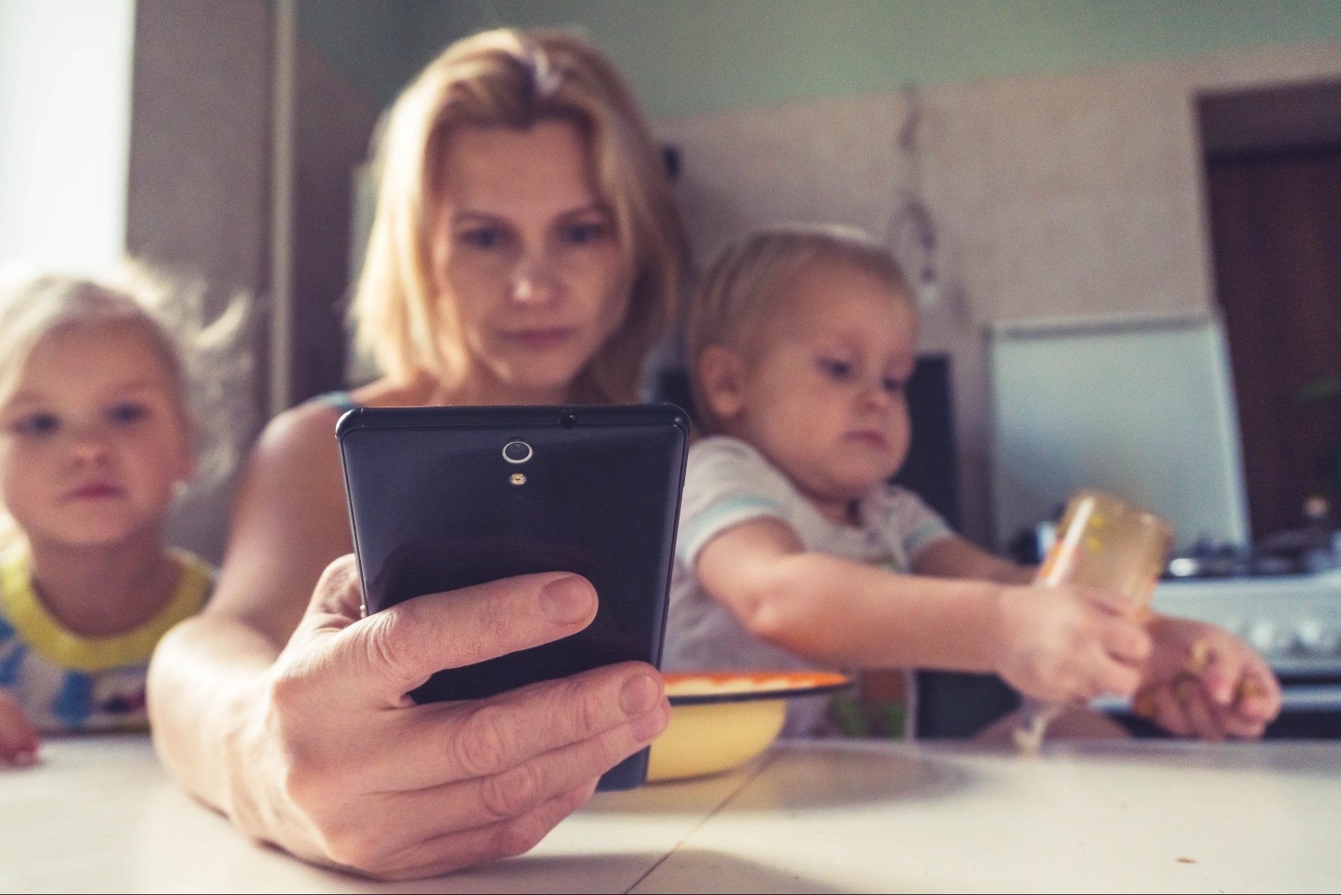Frau mit zwei kleinen Kindern, die aufs Handy schaut
