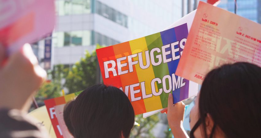 Junge Frau mit schwarzen Haaren hält Regenbogen-Plakat "Refugees welcome" hoch