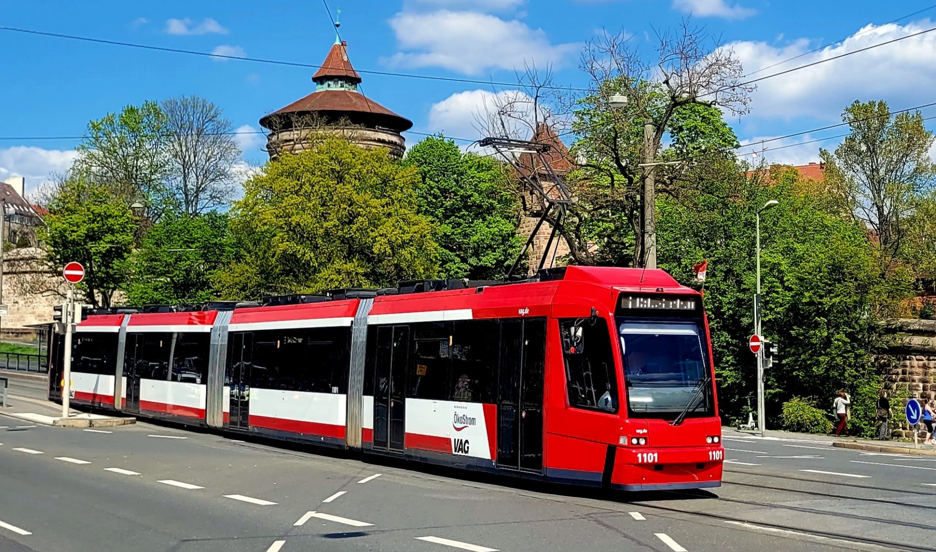 Straßenbahn im Vordergrund, im Hintergrund die Nürnberger Stadtmauer und Bäume.