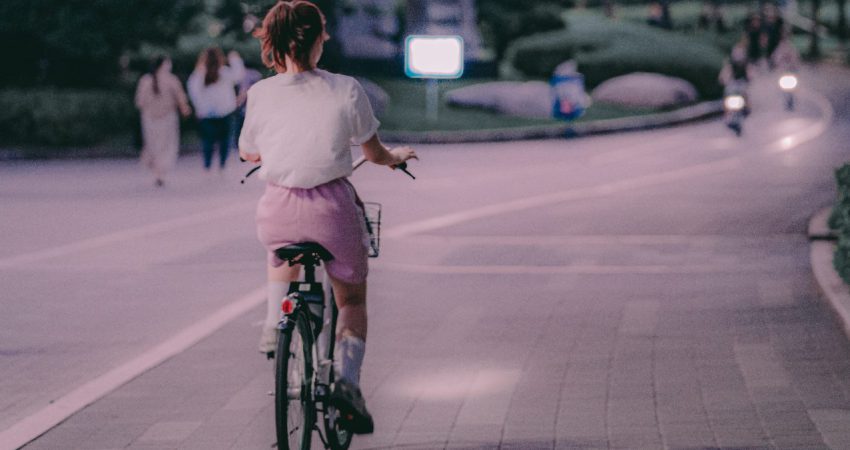 Junge Frau mit Pferdeschwanz fährt mit Fahrrad auf Fahrradweg, Rückansicht