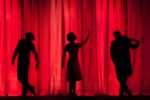 Schattentheater mit drei Personen vor rot erleuchteter Bühne