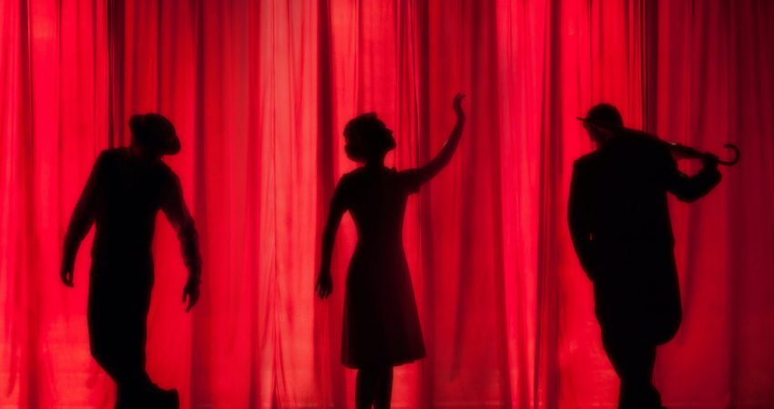 Schattentheater mit drei Personen vor rot erleuchteter Bühne