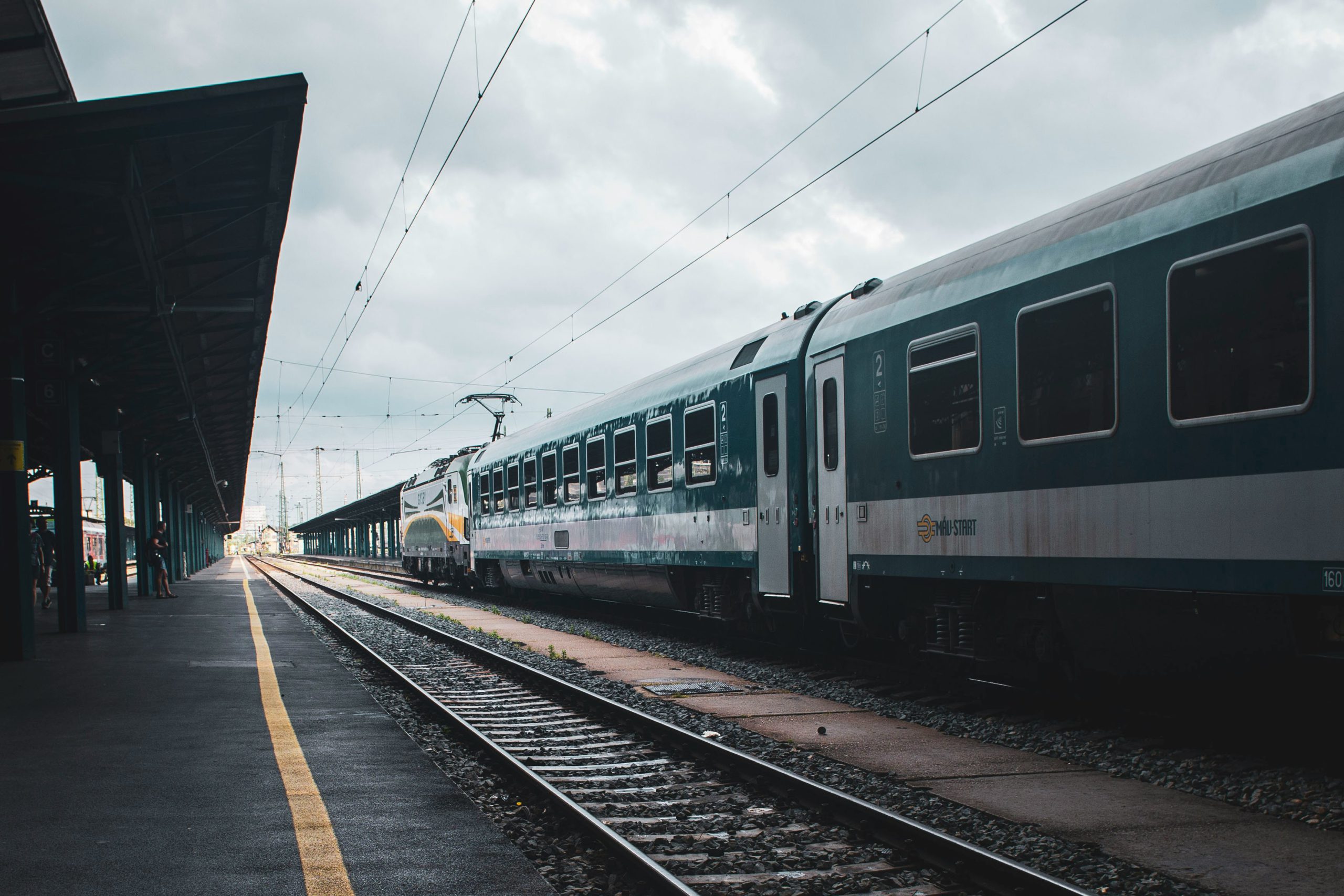 Überdachter Bahnsteig mit zwei Gleisen nebeneinander, auf dem rechten Gleis steht ein grün-weißer Zug