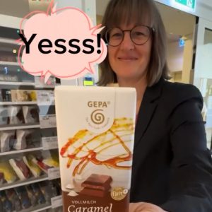 Britta Walthelm probiert den Fair-o-mat in der Kulturwerkstatt auf AEG aus. Sie hält eine Schokolade in der Hand, die sie aus dem Automat gezogen hat. Eine Sprechblase zeigt "Yessss".