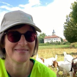 Britta Walthelm mit Sonnenbrille und Cappy, im Hintergrund eine Weide mit Ziegen.