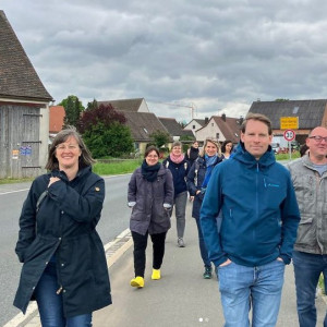 Mehrere Menschen wandern vor dörflichem Hintergrund. Britta Walthelm