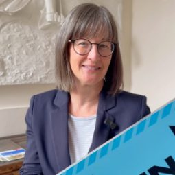 Britta Walthelm hält ein blaues Schild, auf dem Trinkwasserbrunnen steht.